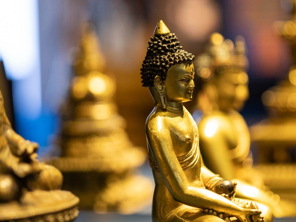 Goldfarbener, sitzender Medizin-Buddha im Profil. In der linken Hand eine Schale, in der rechten Hand eine Frucht. 