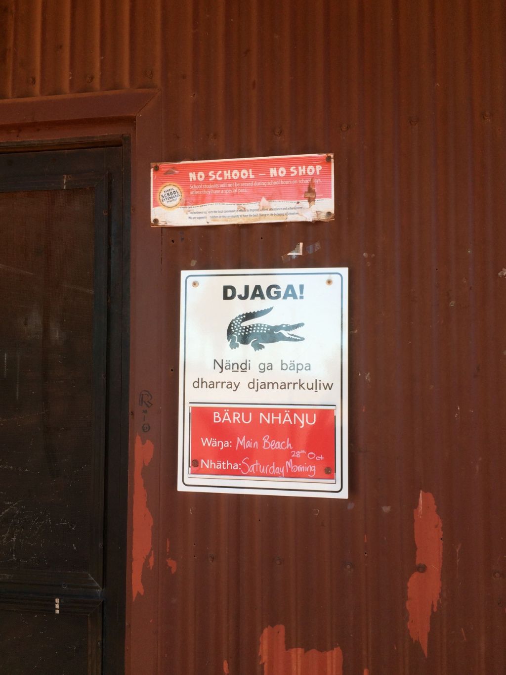 Auf dem Bild ist ein Teil einer Wellblechhütte zu sehen. Neben dem Eingang hängt ein Plakat, das vor Krokodilen warnt.