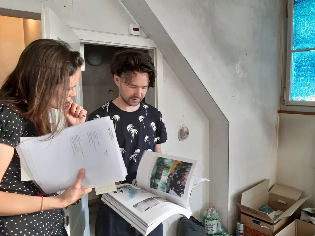 Das Foto zeigt den Künstler Reto Pulfer im Gespräch mit einer Mitarbeiterin des Museums. Er zeigt ihr einen Bildband, den er veröffentlicht hat.