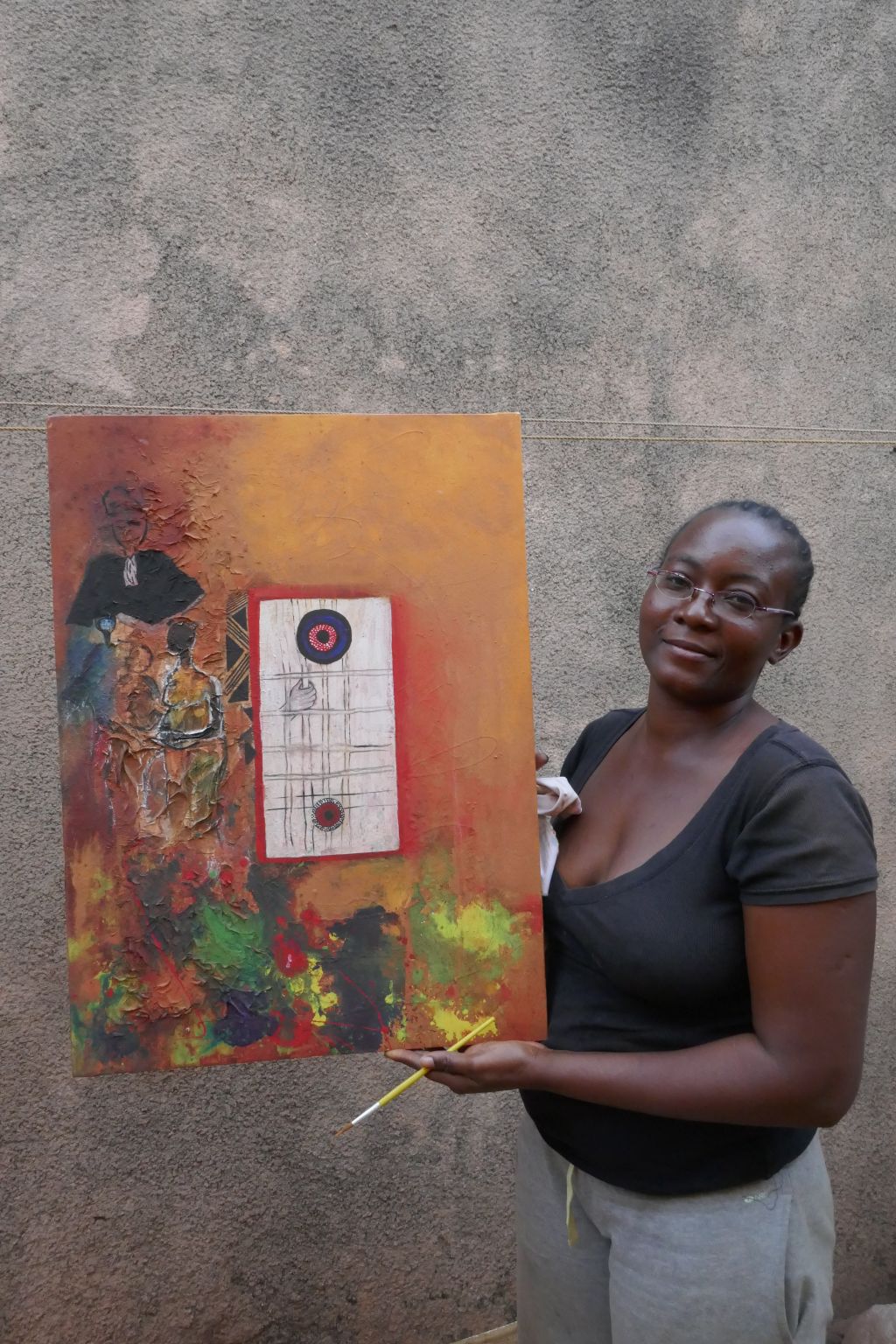 Das Foto zeigt rechts die Künstlerin Safi. Sie steht vor einer Mauer und hält eines ihrer Bilder in die Höhe. Auf orangem Hintergrund ist eine Gefängniszelle zu sehen mit einer Hand an den Gitterstäben. Links davon verschwommen ein Richter, darunter eine Frau und viele Farbkleckse.