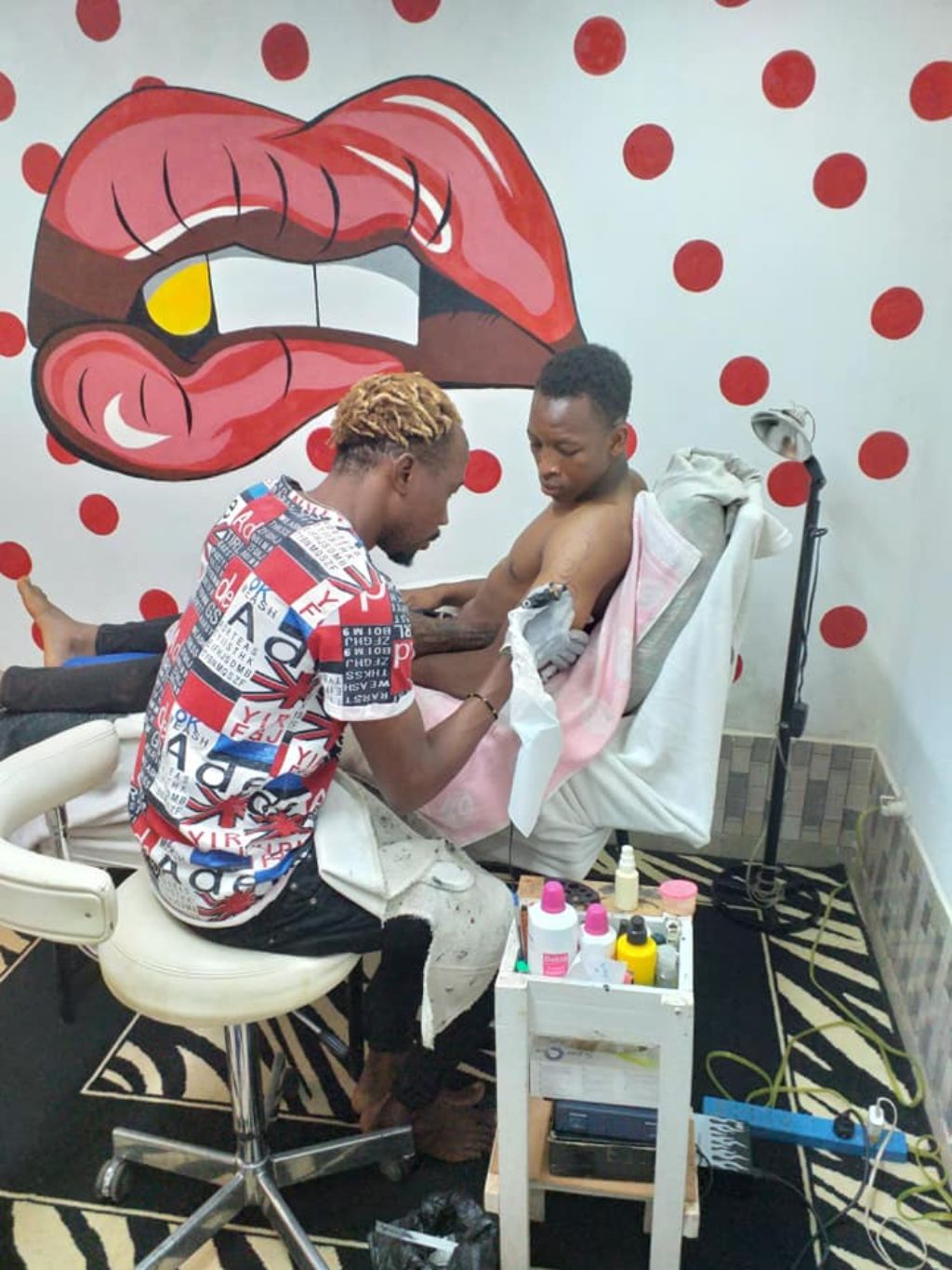 Das Foto zeigt eine Szene in einem Tattoostudio. Der Tätowierer ritzt ein Tattoo in den Arm eines Kunden.