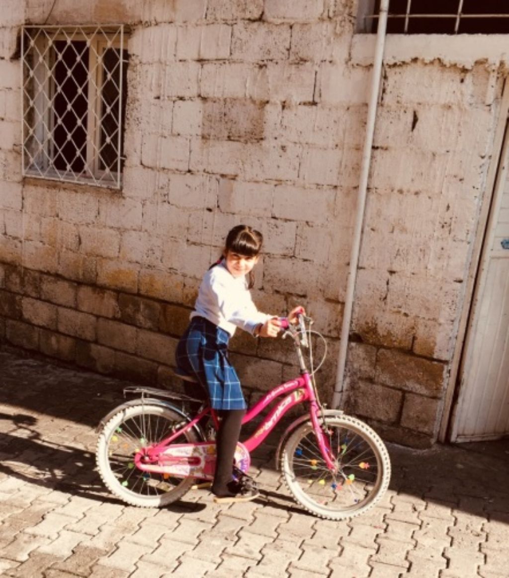 Ein Mädchen fährt vor einem Haus auf ihrem Fahrrad. Das Fahrrad ist rot.