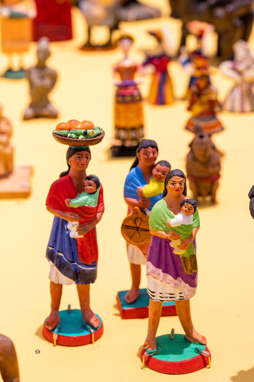 Auf dem Foto stehen drei Figuren im Vordergrund. Es sind drei Frauen aus Südamerika, gekleidet in dortige Trachten, die alle Kinder auf den Armen halten.