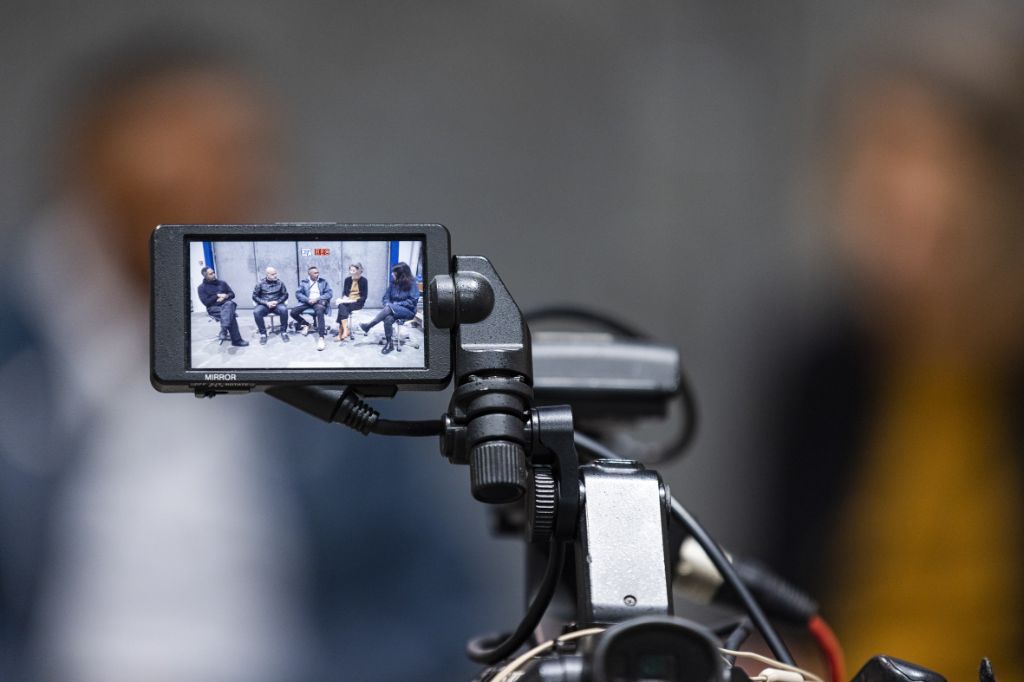 Teil einer Kamera: Auf einem handgrossen Bildschirm sieht man fünf Personen. Der Hintergrund ist verwischt.