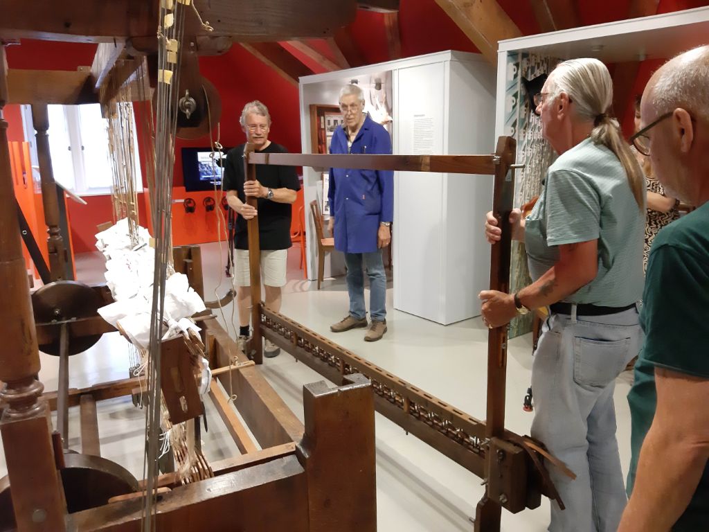 Zwei Männer tragen ein braunes Holzgestell weg. Zwei weitere Männer schauen zu.