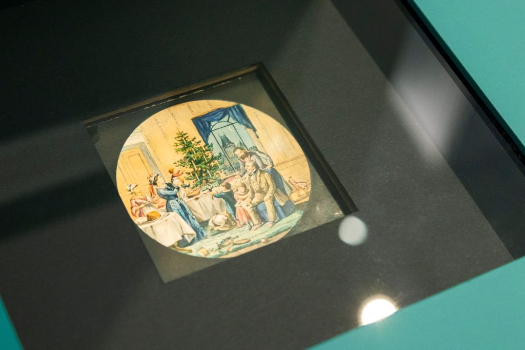 In einem grünen Podest ist eine Vertiefung eingelassen, die mit einer Glasplatte bedeckt ist. Im schwarzen Loch ist ein rundes Bild zu sehen. Es ist eine Zeichnung einer Weihnachtsstube.