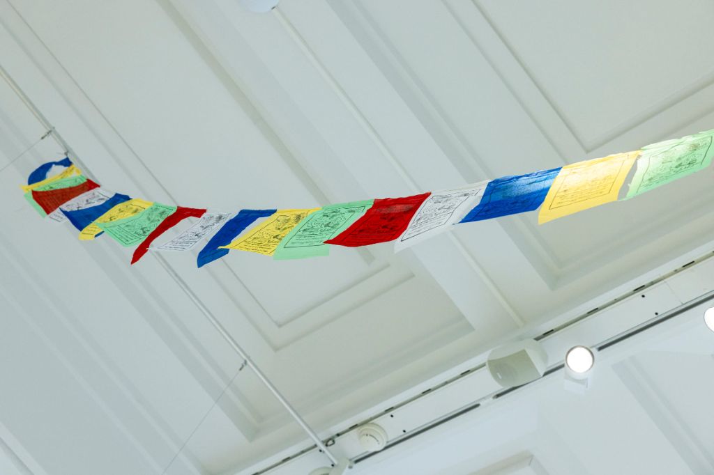 In einem hohen Saal, von dem man die weisse Decke sieht, hängen farbige Zettel an einer Leine.